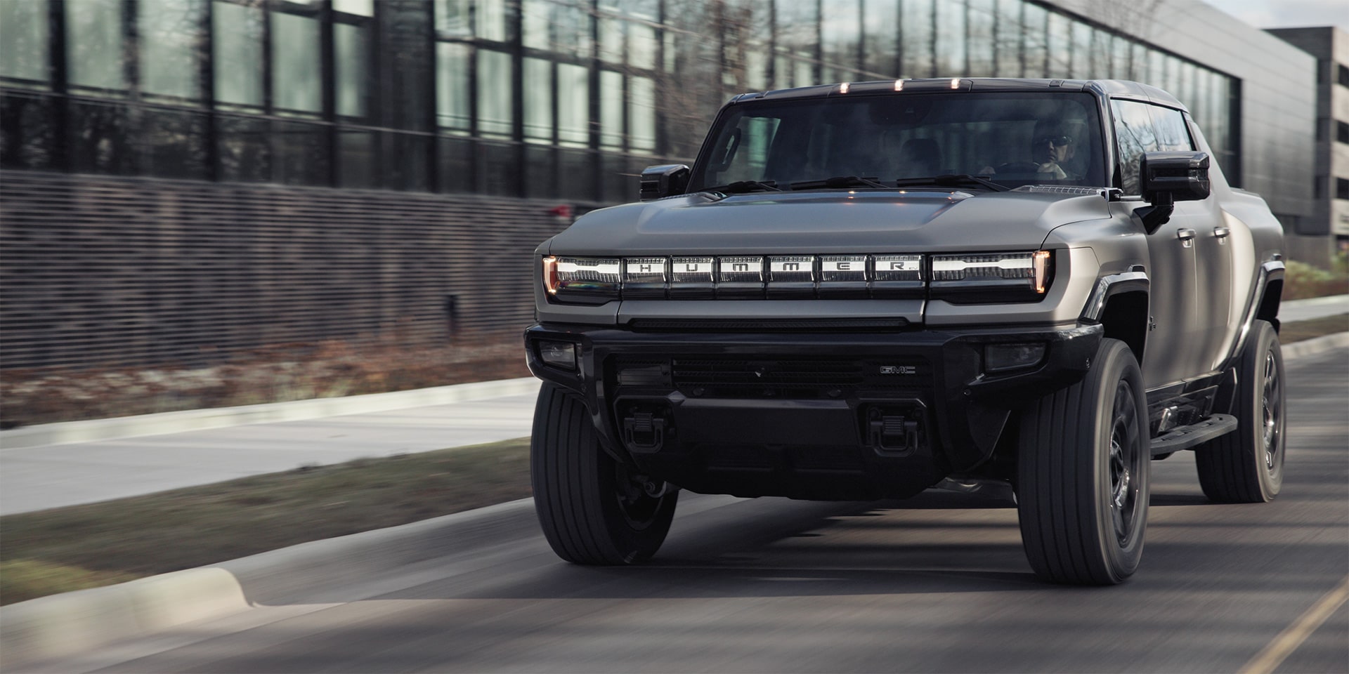 The 2026 GMC HUMMER EV Pickup Truck Driving Past a Business Building