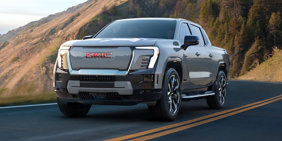Three-quarters View of a 2026 GMC Sierra EV Pickup Truck Driving Through a Mountain Road