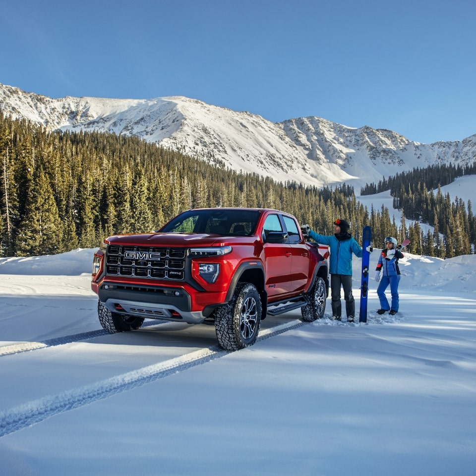 A Couple Unloading Their Skiing Gear From Their GMC Truck with Snow Covered Mountains in the Distance