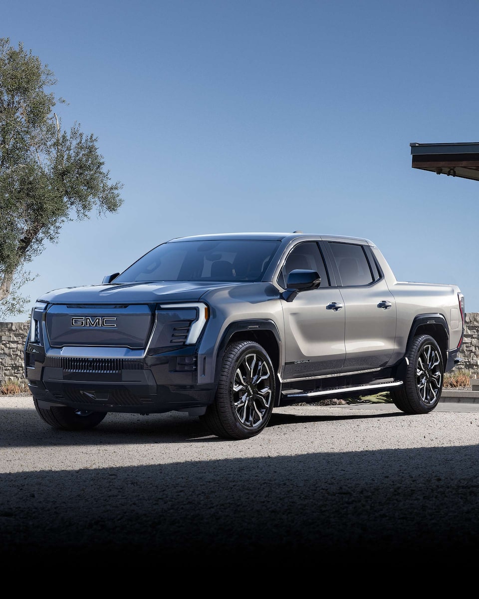 Front Three-Quarters View of a GMC Sierra Denali Edition 1 Electric Truck Driving on an Open Road with Mountains in the Background