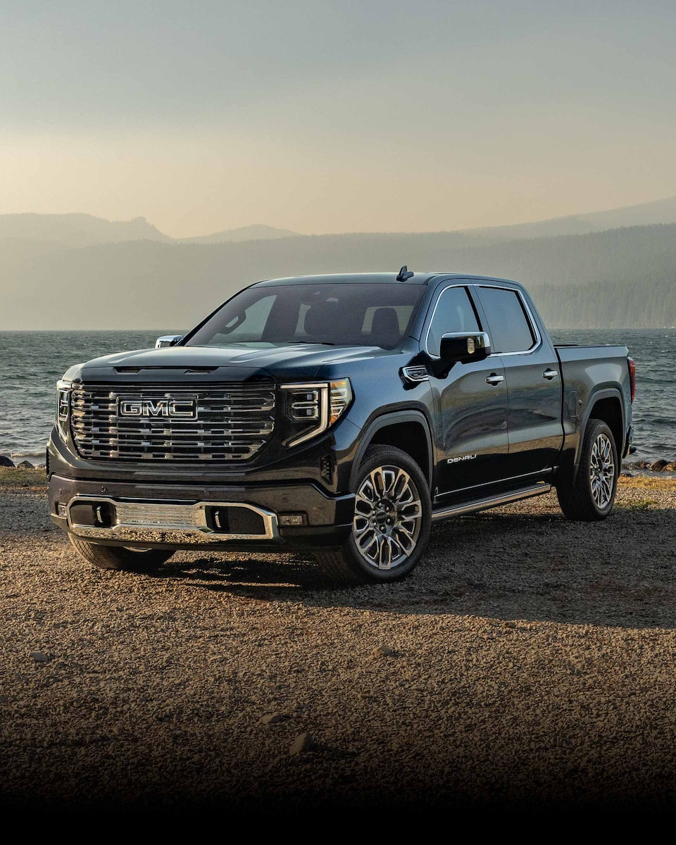 Front Three-Quarters View of a 2024 GMC Sierra 1500 Pickup Truck Parked on a Dirt Path Surrounded by Mountains