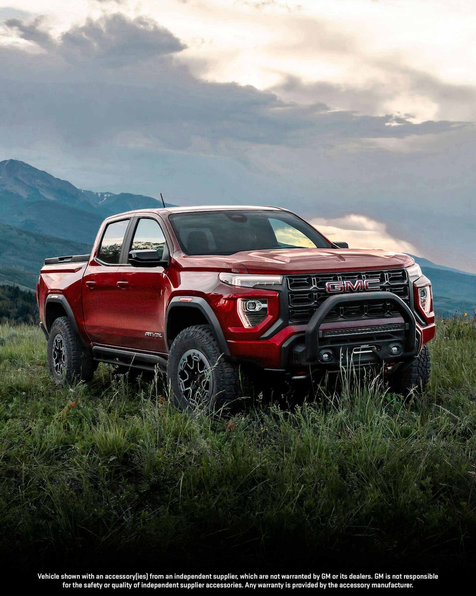 Front Three-Quarters View of a 2024 GMC Canyon Mid-Size Truck Driving on an Open Road at Dusk