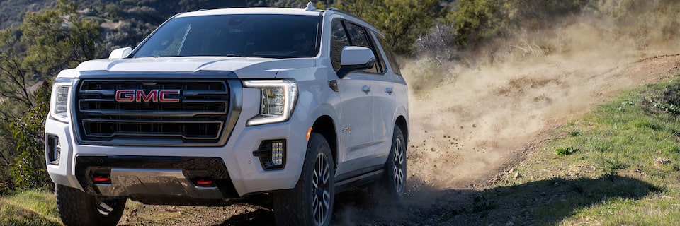 Three-Quarters View of a White GMC SUV Driving Down a Dirt Road