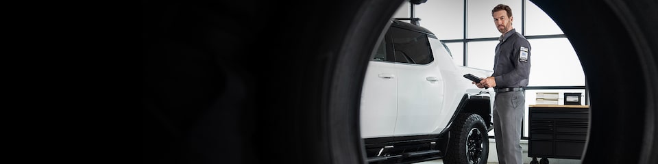 GMC Certified Service Technician Holding a Tablet Standing Next to a Hummer EV Truck