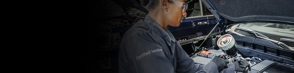 GMC Certified Service Technician Using a Tool to Inspect a Vehicle's Engine Bay