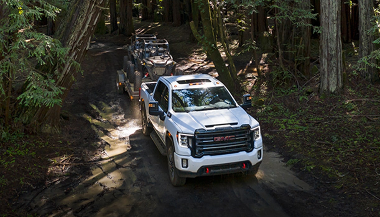 A White GMC Truck Towing an ATV on a Trail