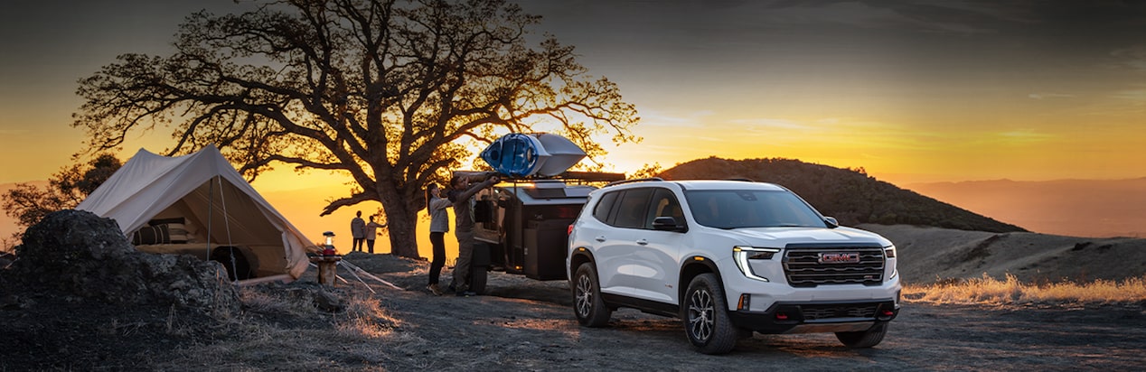 A White GMC SUV with a Cargo Trailer Hitched to It at a Campsite