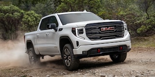 Front Three-Quarters View of the GMC Sierra AT4 1500 Pickup Truck Driving Down a Dirt Road
