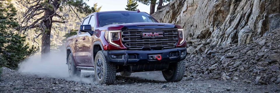 A GMC Sierra 1500 AT4 Truck Kicking Up Dust While Driving on a Gravel Path Next to Mountains