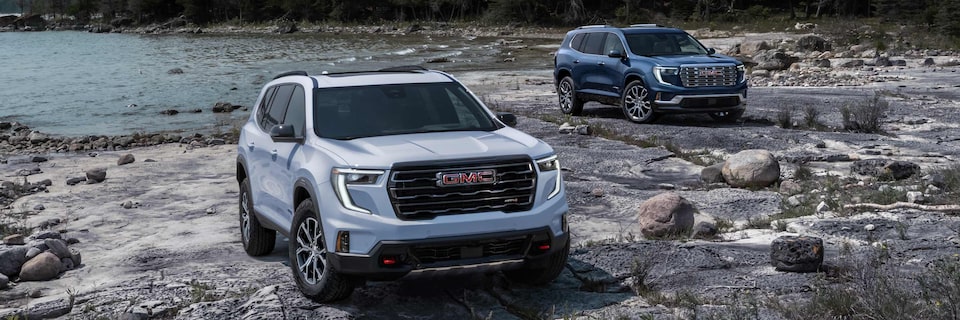 Two GMC Acadia SUVs Parked Together on Rough Terrain with a Lake in the Background