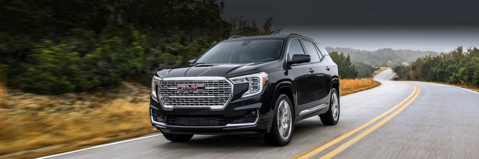 Wide Front Three-Quarters View of a GMC Terrain SUV Driving on an Open Road with Mountains in the Background