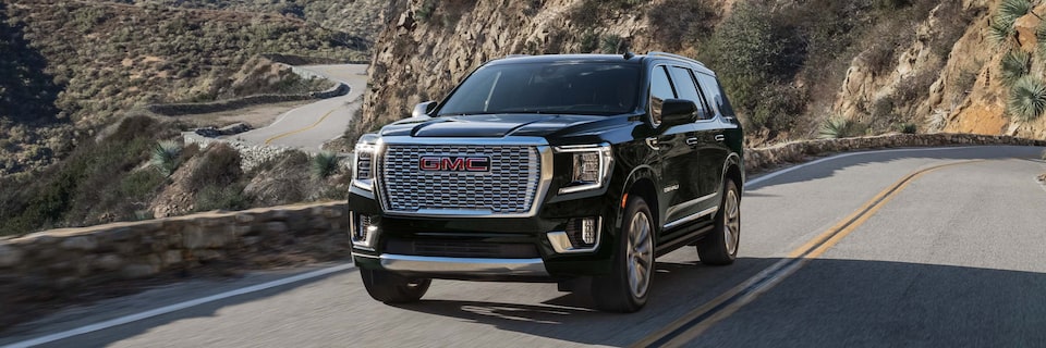 Wide Front Three-Quarters View of a GMC Yukon SUV Driving on an Open Road with Mountains in the Background