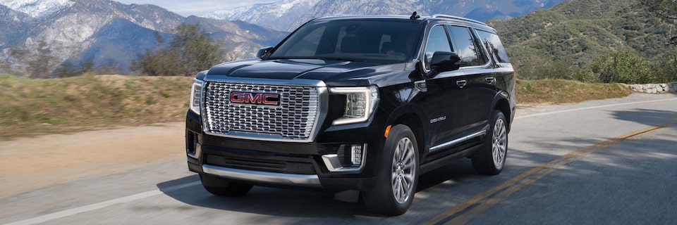 Front Three-Quarters View of a GMC Yukon Denali SUV Driving Down a Road With Mountains in the Background