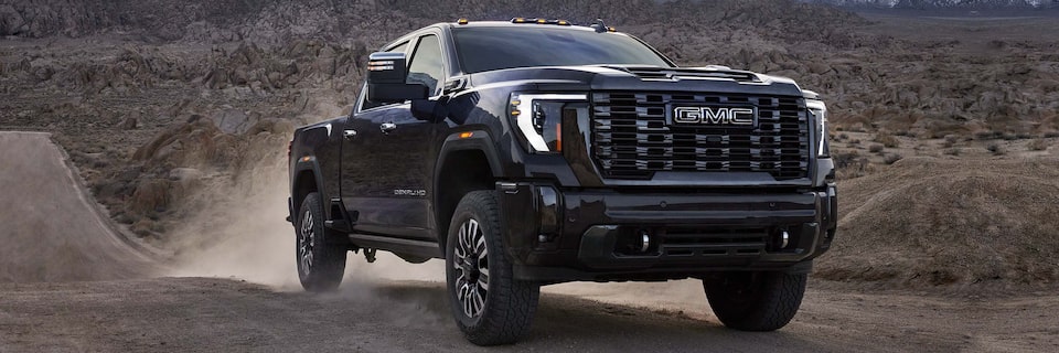 Front Three-Quarters View of a GMC Sierra HD Denali Truck Kicking Up Dust Driving on a Dirt Path Through the Mountains