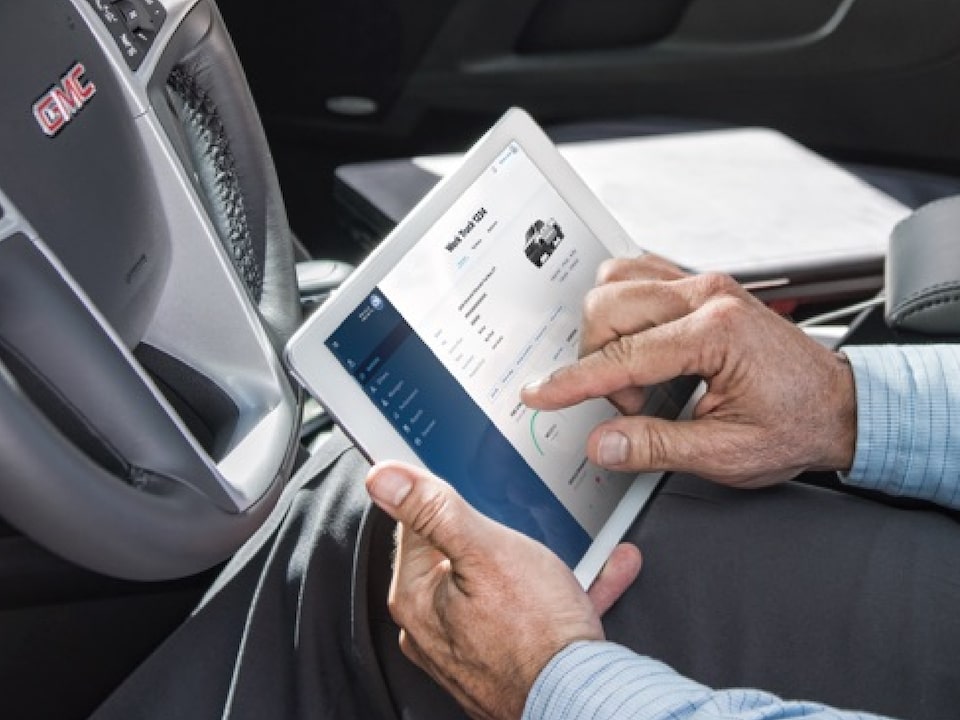 Close-up of a Person Sitting in the Driver's Seat of a GMC Vehicle Using the OnStar Connected Services App on a Tablet