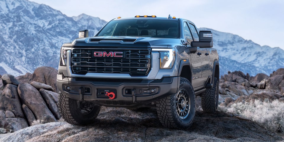 Front Three-Quarters View of a 2025 GMC Sierra HD AT4 Truck Parked in Front of Snow-Covered Mountains