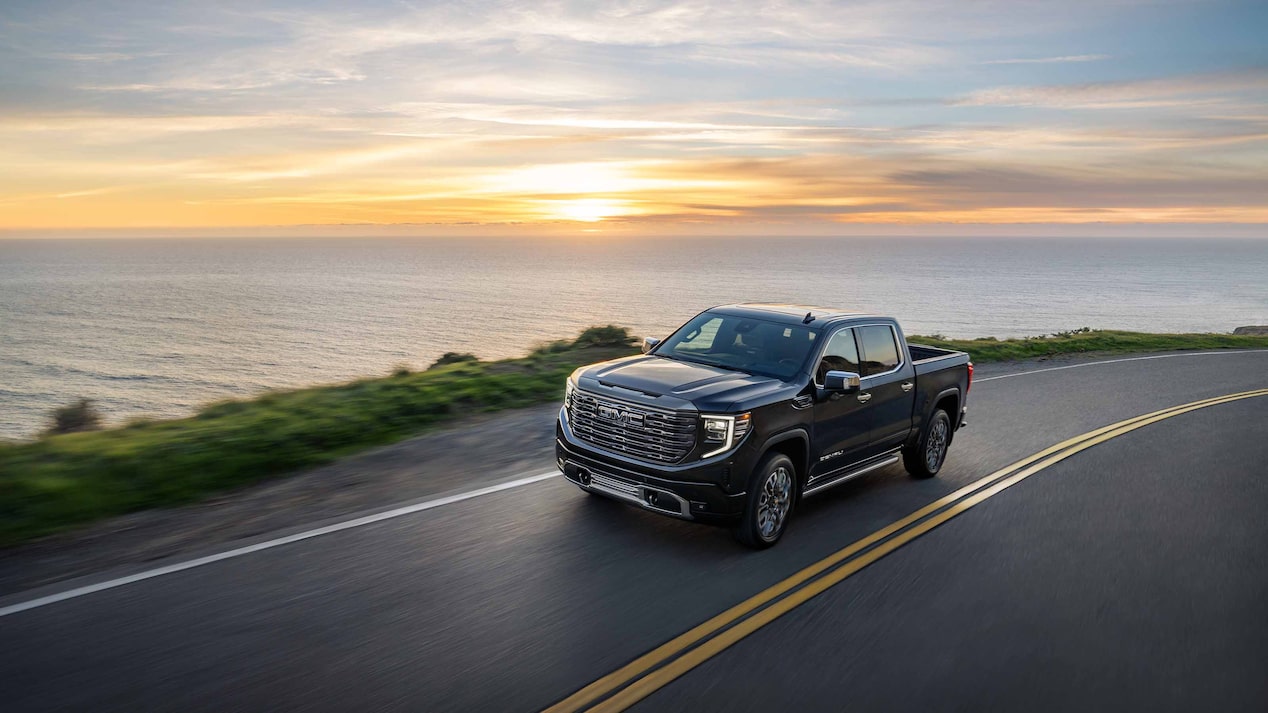 A GMC Sierra Denali Luxury Truck Driving on an Open Road Next to a Lake at Sunset