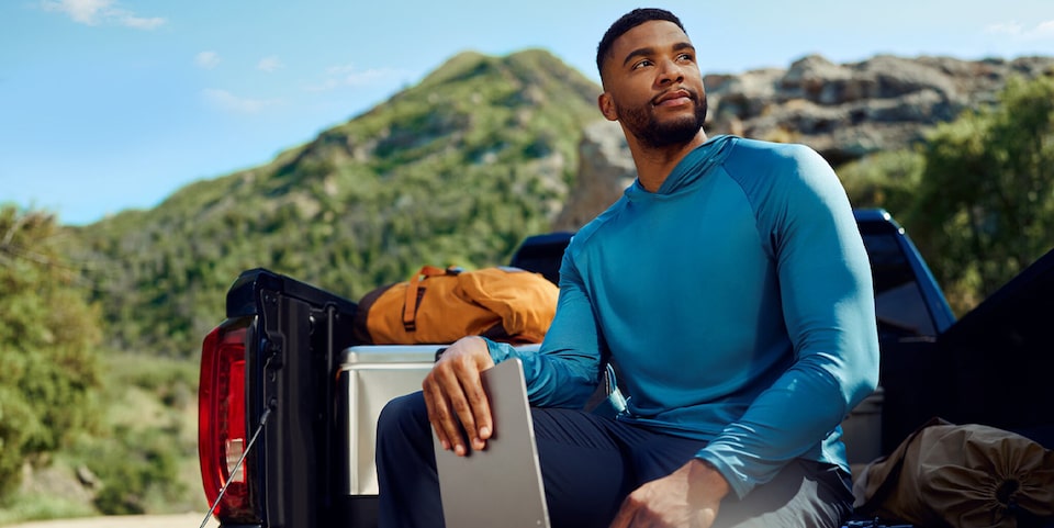 A Man Sitting on the Tailgate of a Truck Looking Into the Distance and Holding a Tablet