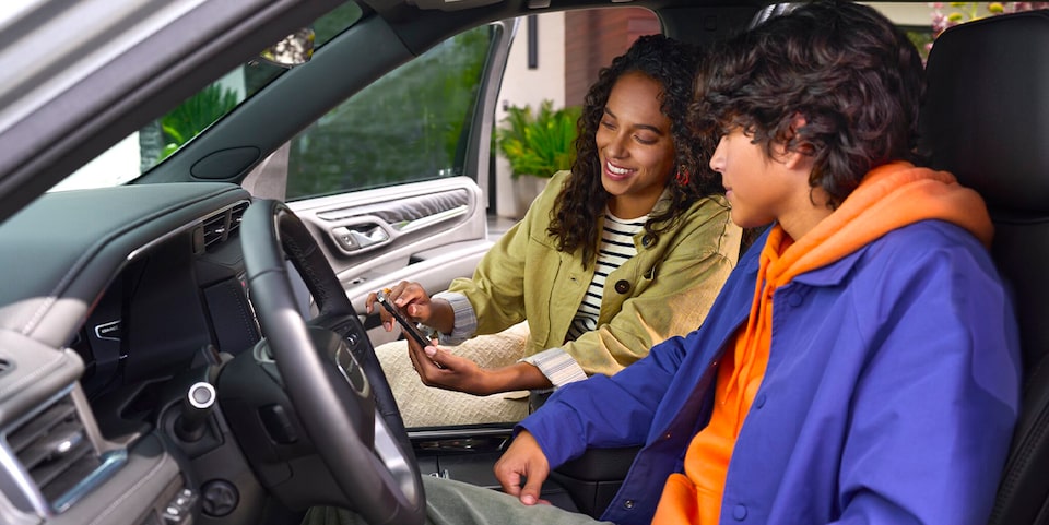 A Teenager Sitting in the Driver's Seat of a Vehicle While Looking at a Smartphone Held by a Passenger