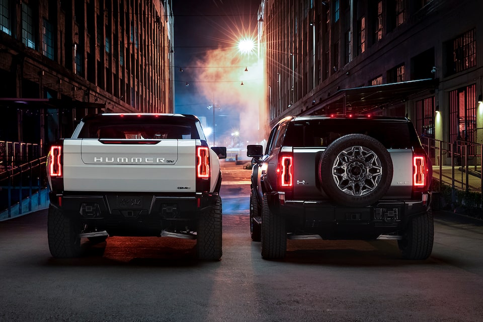 Rear View of a HUMMER EV Pickup Truck and a HUMMER EV SUV Parked in a City Alleyway at Night with a Street Light Shining