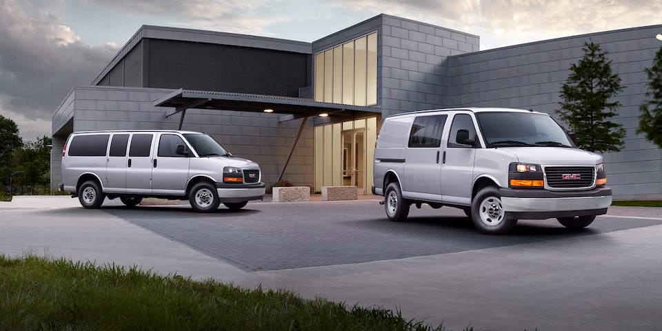 Two GMC Savana Cargo Van's Parked in Front of a Building