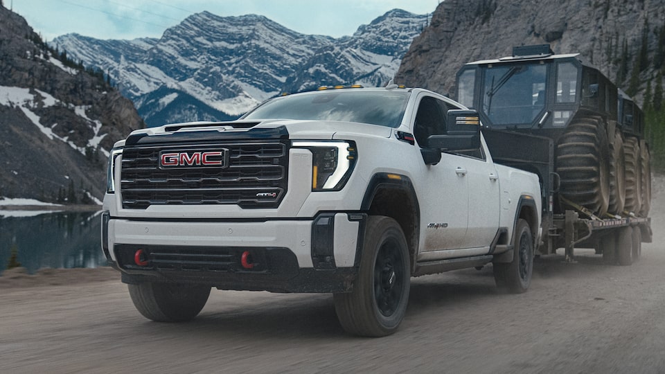 Close-Up Front Three-Quarters View of a GMC Sierra HD AT4 Truck Hauling a Trailer Through Snow-Covered Mountains