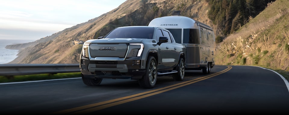 Close-up Front Three-Quarter View of the GMC Sierra EV Truck Hauling an RV on a Highway