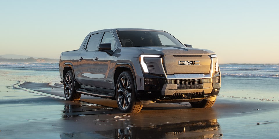 Front Three-Quarter View of the Sierra EV Pickup Truck Driving Down the Beach at Sunset